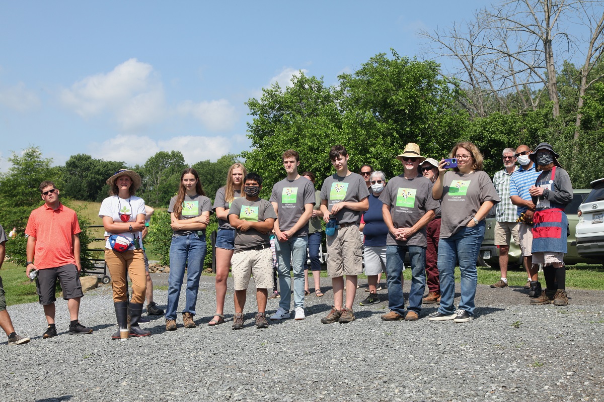 The AFLO team posing for a picture. Most have AFLO shirts on.  Some have face masks.  Trees are in the background