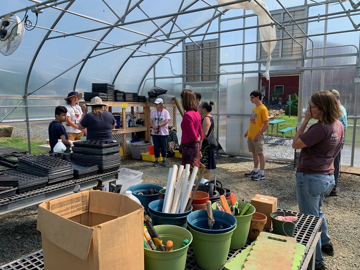 People in the Greenhouse.  There are buckets of tools and  garden trays stacked neatly