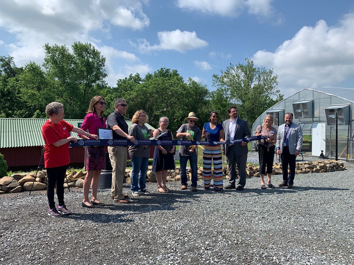 People standing in front of a large ribbon signaling the start of a new farm
